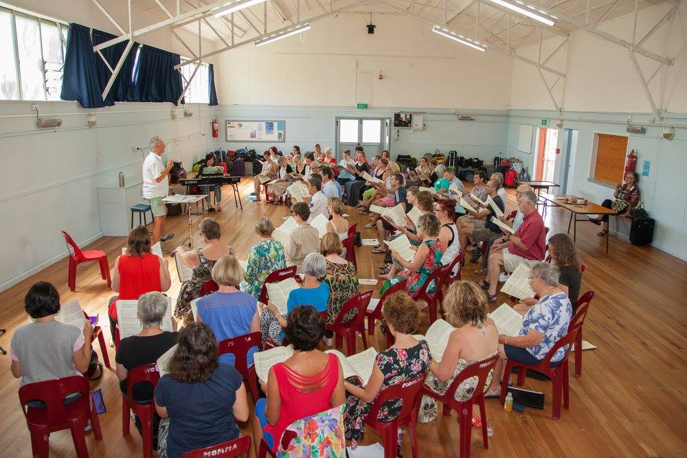 Picture of several choir members in relaxed clothes in during a rehearsal in a venue on Waiheke island